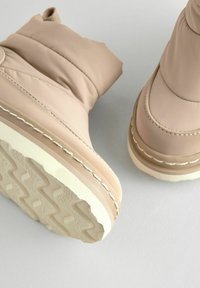 Beige geïsoleerde enkellaarsjes met een gladde, gevoerde textuur, voorzien van een witte rubberen zool en een zigzagloopvlak.