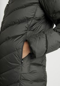 Mörkgrön vadderad jacka med quiltad design, utrustad med en dragkedjeförsedd ficka och elastiska muddar för en tajt passform. Mjukt, vattenavvisande material.