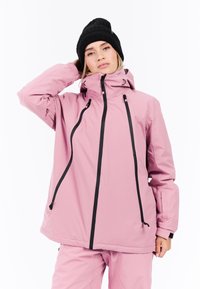 Roze waterdichte jas met een hoge kraag, zwarte ritsen en verstelbare trekkoorden. Gladde textuur, gecombineerd met een zwarte gebreide beanie.