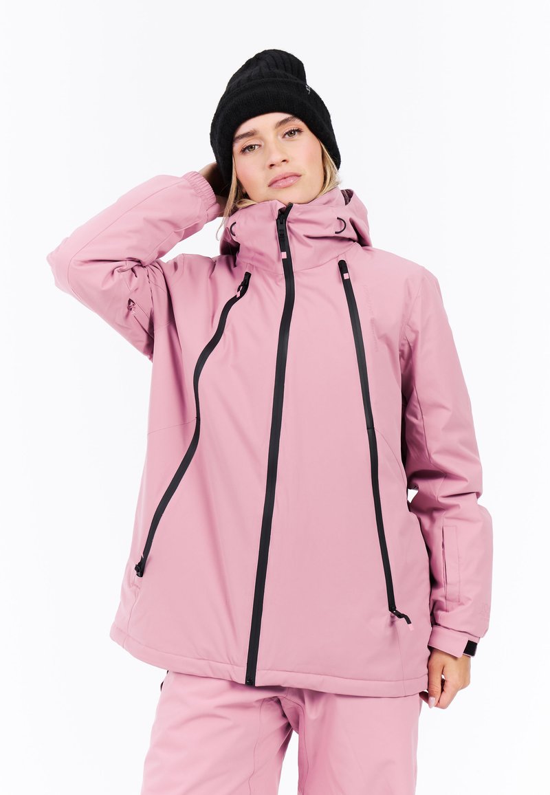 Roze waterdichte jas met een hoge kraag, zwarte ritsen en verstelbare trekkoorden. Gladde textuur, gecombineerd met een zwarte gebreide beanie.