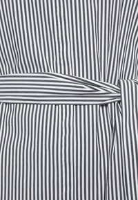 Pruhovaný oděv s kombinací černých a bílých vertikálních pruhů, s opaskem na zavázání v pase a hladkou texturou látky.