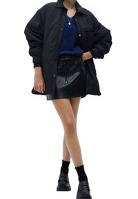 Sort oversized skjortejakke over en blå sweater, parret med en sort læder-mini-skjørt. Sorte chunky loafers og ankelstrømper fuldender looket.