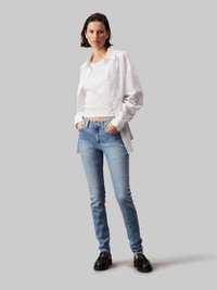 Fehér gombos ing egy fehér cropped top felett, világoskék skinny farmernadrággal és fekete loaferekrel párosítva. Sima textúrák, laza dizájn.