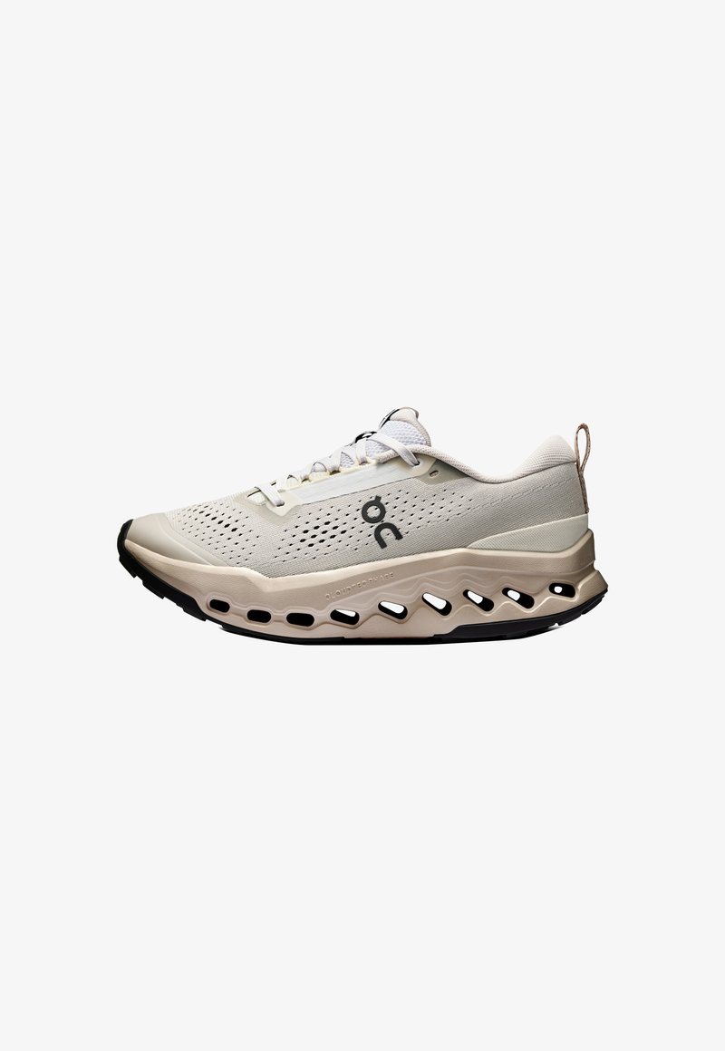 Baskets de sport beige et crème avec tige perforée, semelle rembourrée, logo noir et languette sur fond blanc.