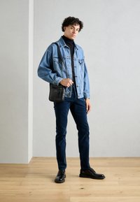 Denim jakna svetlo modre barve, črna majica z ovratnikom, temno modri hlače in črne čevlje. Drži majhno črno torbico z zadrgo.