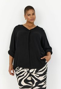 Blouse noire ample avec un col en V et des manches retroussées. Associée à un pantalon à rayures zébrées blanches et noires.