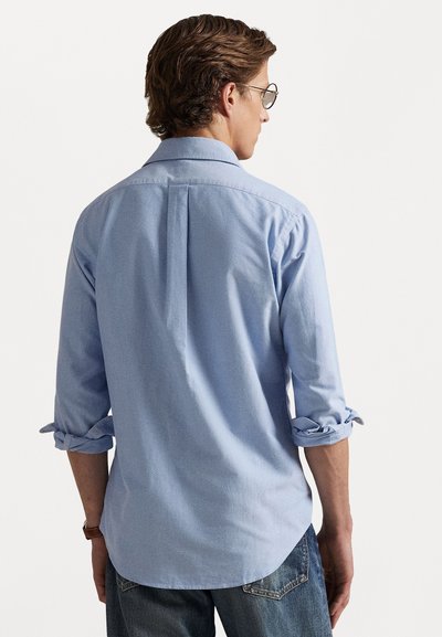 Gaišzils krekls ar garām piedurknēm, kas saritinātas pie aprocēm, ar taisnu apakšmalu un aizmugures plisējumu. Mīksta auduma tekstūra.