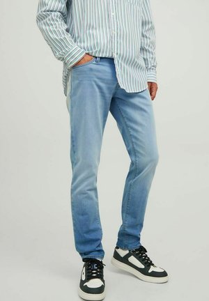 Vaqueros de mezclilla azul claro con corte slim, que cuentan con cinco bolsillos y un desvanecimiento sutil. Combinados con zapatillas negras y blancas.