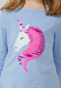 Jasnoniebieska koszula z długim rękawem z wzorem jednorożca wykonanym z cekinów w kolorach białym, różowym i fioletowym, o fakturowanej i błyszczącej powierzchni.