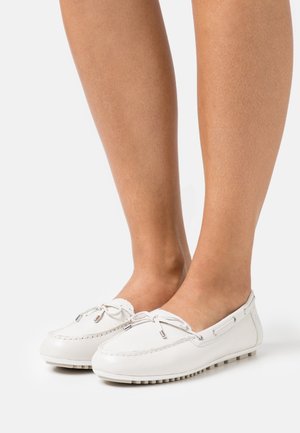 Mocassins blancs en cuir à enfiler avec détails en nœud portés pieds nus, montrés sous des angles latéraux et avant contre un fond blanc uni.