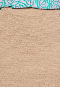 Saia texturizada bege com um padrão estriado, combinada com uma blusa estampada em rosa e verde-água com formas abstratas semelhantes a folhas.