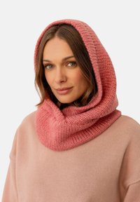 Różowy, dziany szal-kapa o teksturowanym wzorze, noszony na jasnoróżowym swetrze. Gładki materiał, tworzący przytulny wygląd.