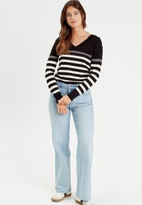 Top de rayas en blanco y negro de manga larga con escote en V y detalles plateados, combinado con vaqueros de tiro alto en azul claro y zapatillas blancas.