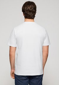 Biała bawełniana koszulka, krótki rękawek, okrągły dekolt. Gładka tekstura, prosty design bez widocznych logo lub wzorów. Wyświetlony widok z tyłu.