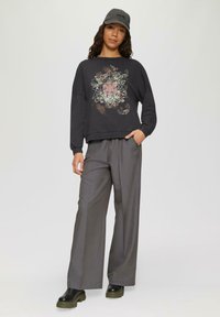 Czarny oversized sweatshirt z geometrycznym kwiatowym wzorem, zestawiony z szarymi spodniami typu wide-leg i czarnymi platformami. Czapka noszona tyłem.