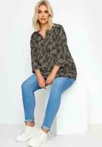 Czarna bluzka w wielokolorowy wzór o luźnym kroju, z dekoltem w kształcie litery V i rękawami o długości trzy czwarte, zestawiona z jasnoniebieskimi rurkami i białymi sneakersami.