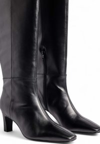 Botas de cuero negro hasta el tobillo con punta afilada, tacón de bloque moderado y detalle de cremallera lateral. Textura suave con costuras mínimas.