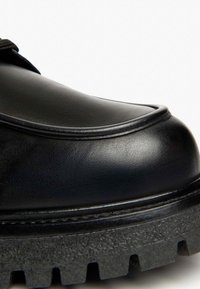Schwarze Lederschuhe mit glatter Oberfläche, runder Zehenform und kontrastierender, strukturierter Gummisohle mit tiefen Profilen für besseren Halt.