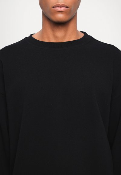 Sweatshirt noir en tissu doux, doté d'un col rond classique et d'une coupe décontractée avec des manches longues, sans motifs ni accents visibles.
