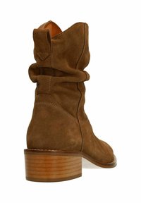 Brown suede ankle boot with a slouchy design, rounded toe, and stacked wooden heel. Features stitching detail and a pull tab at the back.