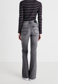 Jeans acampanados grises de mezclilla con bolsillos traseros bordados, combinados con una camiseta de manga larga a rayas en blanco y negro.