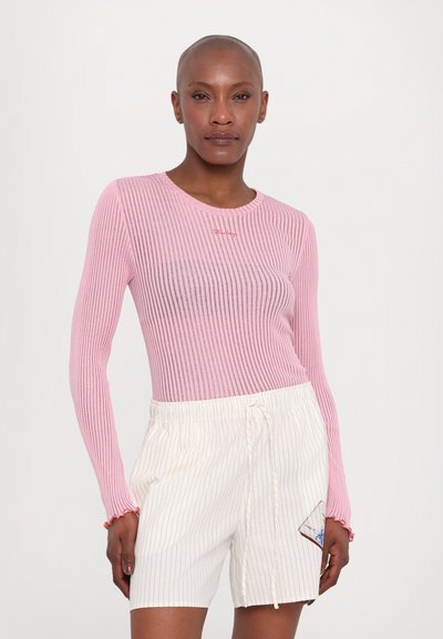 Ribbet langermet topp i lys rosa med rund hals og dekorativ søm. Kombinert med hvite shorts med tynne striper og broderte detaljer.
