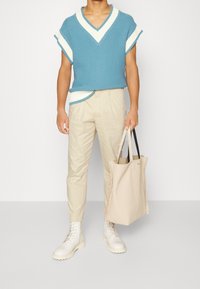 Maglione blu a maniche corte lavorato a maglia con dettagli bianchi, pantaloni beige a gamba affusolata, stivali crema stringati e una morbida borsa a tracolla beige.