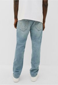 Jeans de mezclilla azul claro con un corte relajado, que cuentan con bolsillos traseros con detalles de costura. Terminados con un ligero desvanecimiento y zapatillas blancas.