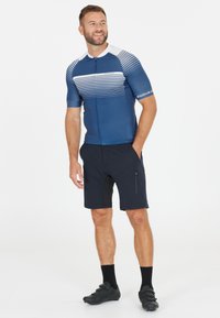 Miestenska cyklistická dres v námorníckej modrej s horizontálnymi bielymi pruhmi; v kombinácii s tmavými šortkami. Obsahuje zips a vrecká; vyrobený z elastického materiálu.