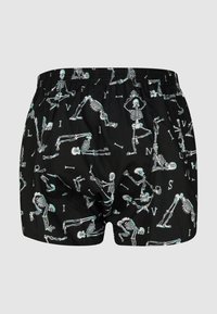 Schwarze Boxershorts mit einem Muster aus weißen Skeletten in verschiedenen Yoga-Posen sowie kleinen verstreuten Knochen und Buchstaben.