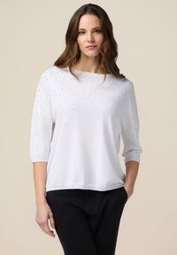 Maglione bianco con maniche a tre quarti, caratterizzato da un motivo a pois di strass, texture morbida e vestibilità comoda.