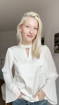 Blusa bianca con colletto alto e dettaglio a occhiello, caratterizzata da un corpo in satin liscio e maniche lunghe a pieghe con texture. In vista dei pantaloni in denim casual.