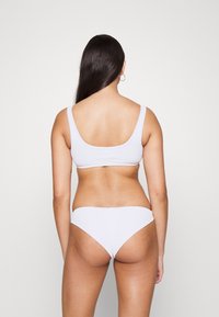 Conjunto de bikini branco com texturas em relevo, apresentando um top tipo tank e uma parte de baixo de cintura baixa, confeccionado em material suave com um design simples e sem costuras.