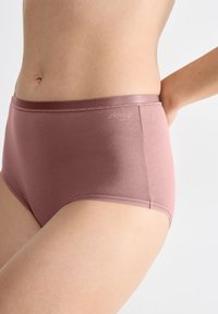 Vrouw in een hoog- taille mauve naadloze katoenen ondergoed, staand met één hand achter haar rug tegen een neutrale achtergrond.