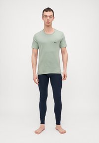 Ljusgrön bomullströja med korta ärmar, prydd med en liten svart logotyp på framsidan. Matchad med åtsittande marinblå leggings. Barfota.