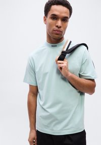 Ανοιχτό πράσινο κοντομάνικο μπλουζάκι σε στυλ μέντας με το λογότυπο "BOSS" στον γιακά, συνδυασμένο με μαύρο σορτς και τσάντα με λουρί στον ώμο.