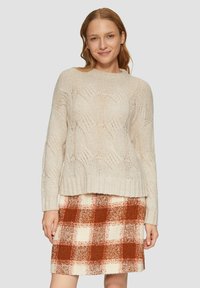 Jasno beżowy sweter z dzianiny z teksturowanym wzorem fal. W zestawieniu z mini spódnicą w kratę w kolorach pomarańczowym, kremowym i rdzawego.