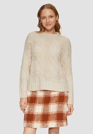 Pull en tricot beige clair avec un motif de vagues texturé. Assorti à une jupe mini à carreaux dans des teintes d'orange, de crème et de rouille.