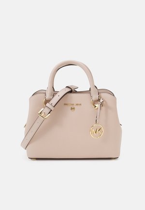 Sac à main beige Michael Kors avec doubles poignées, bandoulière réglable et breloque logo dorée sur fond uni.