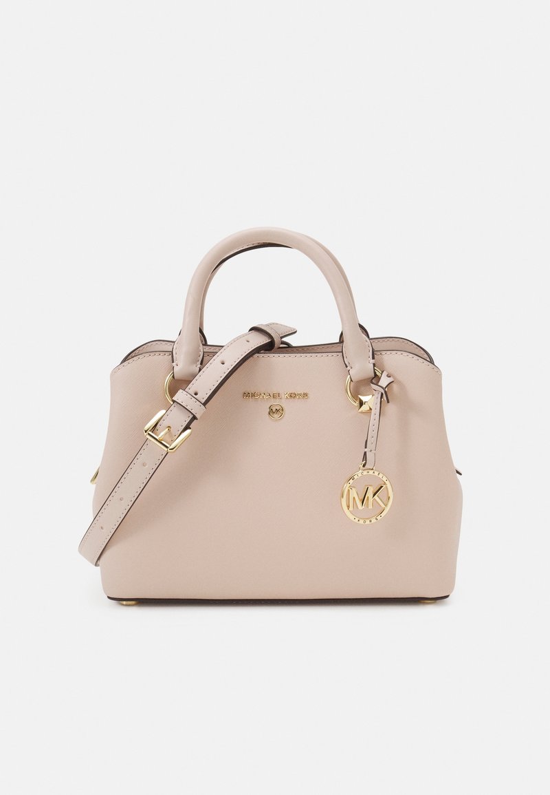 Sac à main beige Michael Kors avec doubles poignées, bandoulière réglable et breloque logo dorée sur fond uni.