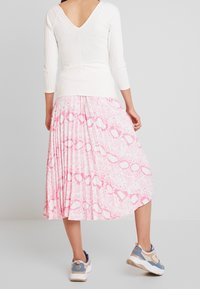 White ribbed top with a v-neck, paired with a pink pleated skirt featuring a circular pattern. Model wears blue and beige sneakers.