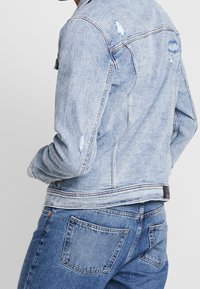 Ljusblå denimjacka med slitna detaljer, klassisk passform, stickade sömmar och knäppt fram. Texturerad tyg och två sidofickor.