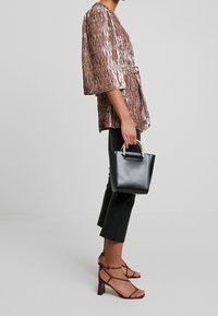 Bronsfärgad topp med struktur, kort ärm och bälte, tillsammans med svarta slim fit-byxor och en liten svart handväska med guldhandtag. Bruna klackar med remmar.