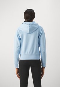 Sudadera con capucha de color azul claro, hecha de una tela suave, con puños acanalados, capucha con cordón y un corte relajado, combinada con leggings negros.