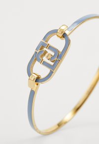Gouden armband met een blauwe emaille accent. Het ontwerp heeft een ovale sluiting met ineengestrengelde vormen en gladde, gebogen randen.