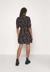 Černé květinové šaty s krátkými nabíranými rukávy, s přiléhavým pasem a sukní ve stylu skater. Tkanina je pokryta malými barevnými květy.