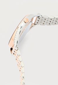 Πλάγια όψη ενός δίχρωμου μεταλλικού ρολογιού χειρός με μπρασελέ από αλυσίδα σε ασημί και ροζ χρυσό και με ανάγλυφη κορώνα στην κάσα.