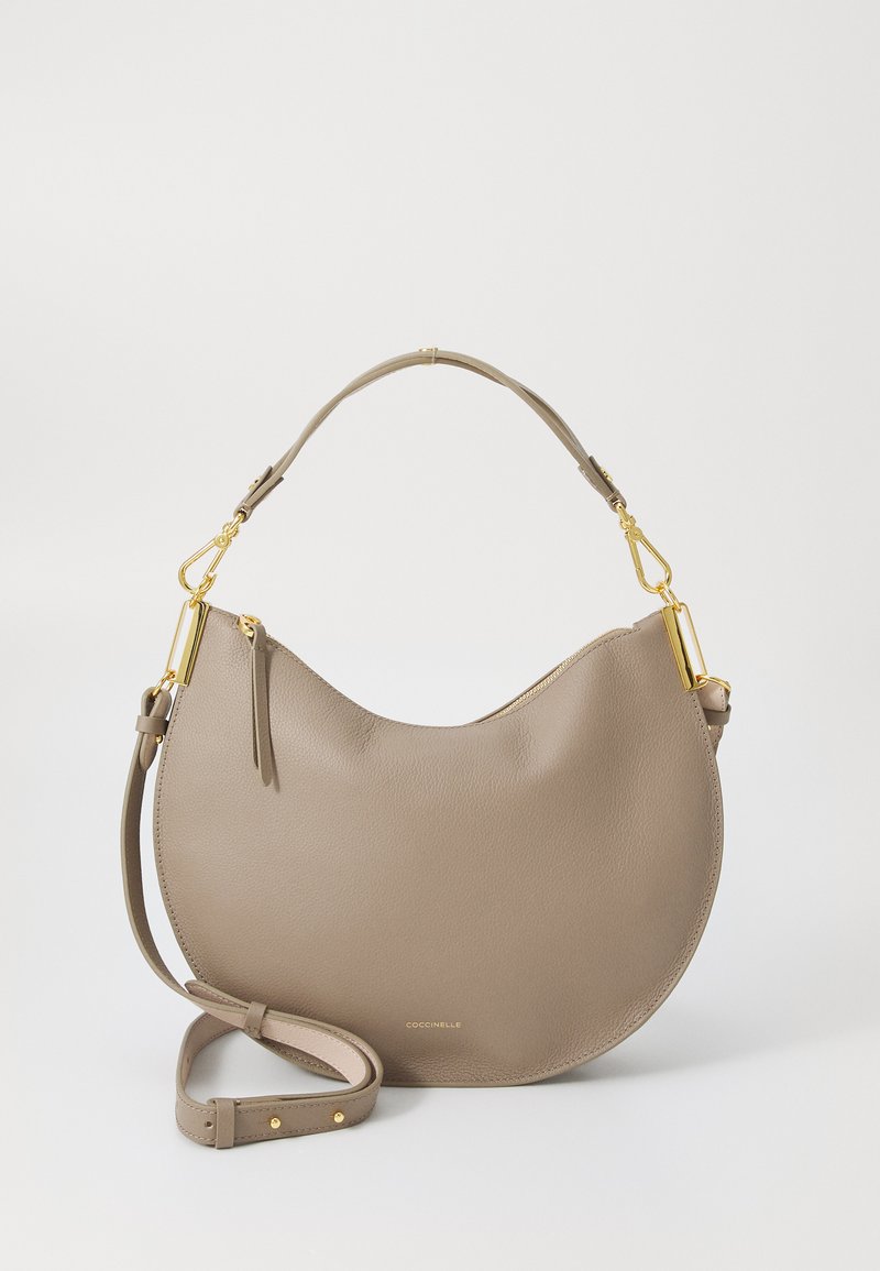 Bolsa de mão em couro castanho com forma curvada, ferragens em tom de ouro e alça destacável. Textura suave e design minimalista.