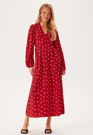 Robe maxi rouge à fleurs avec un décolleté en V, de longues manches ballon et une silhouette fluide, ornée de motifs de fleurs blanches.