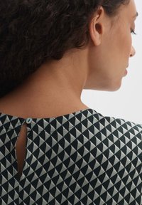 Blusa con motivo geometrico in nero e crema, con dettaglio a chiusura a chiave sulla schiena e bottoncino blu.